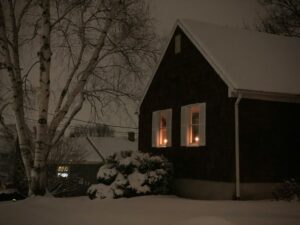 Winter evening scene of home with candles in the window representing challenges of pest control in the winter season.