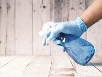 Close up of someone's gloved hand about to spray a cleaning solution from a bottle, representing spring cleaning.