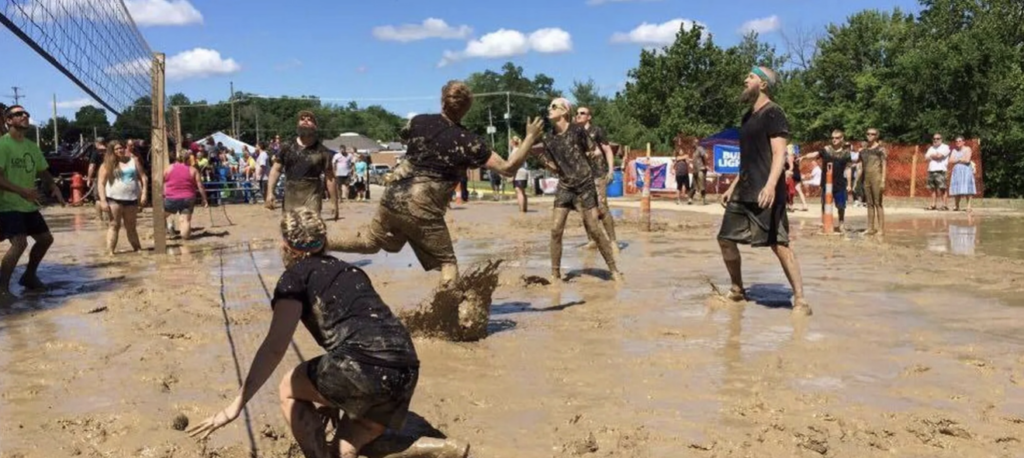 People playing volleyball in the mud at a community event hosted in downtown Otsego