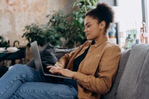 A woman siting at home on a couch with a laptop, representing researching to make a decision.