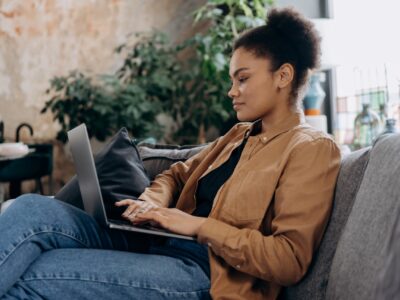 A woman siting at home on a couch with a laptop, representing researching to make a decision.