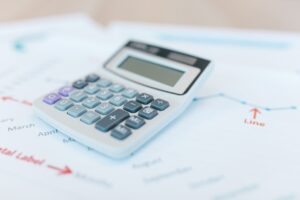 Close up of a calculator on top of various report papers indicating evaluating cost and value to make a decision. 